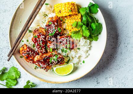 Concept alimentaire asiatique. Poulet au sésame avec riz et légumes dans une assiette, fond gris. Banque D'Images