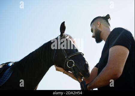 Homme arabe grande barbe porter en noir avec le cheval arabe. Banque D'Images