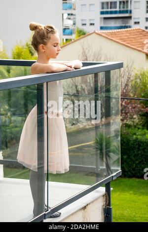 Jeune fille pensive rêvante portant une robe de danse. Enfant caucasien debout sur le balcon de la maison, regardant sur le côté réfléchi. Banque D'Images