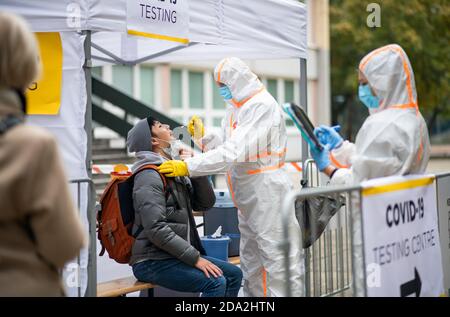 Jeune homme dans le centre d'essai Covid-19 dehors sur la rue, coronavirus et prenant écouvillon de la bouche concept. Banque D'Images