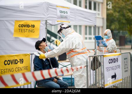 Jeune homme dans le centre d'essai Covid-19 dehors sur la rue, coronavirus et prenant écouvillon de la bouche concept. Banque D'Images