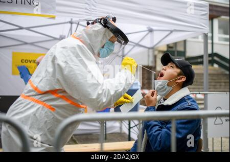 Jeune homme dans le centre d'essai Covid-19 dehors sur la rue, coronavirus et prenant écouvillon de la bouche concept. Banque D'Images