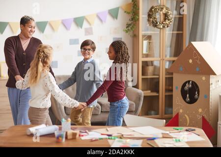 Portrait d'une femme afro-américaine souriante tenant la main avec des enfants tout en dansant pendant la leçon à l'école, espace de copie Banque D'Images