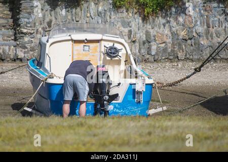 Un propriétaire de bateau travaillant sur son petit bateau à moteur amarré sur la rivière Gannel à marée basse à Newquay en Cornouailles. Banque D'Images