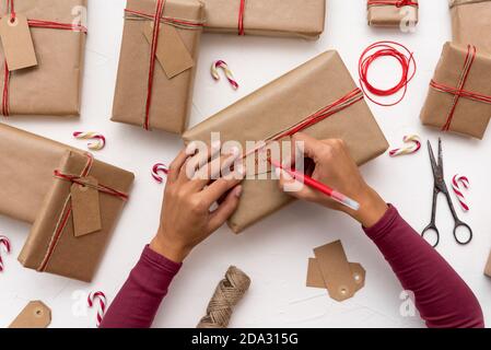 Les mains des femmes écrivent des cartes de Noël sur des boîtes-cadeaux décorées avec papier kraft Banque D'Images