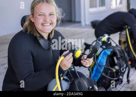 Des plongeurs se dressent et vérifient leur équipement, une fille regardant l'appareil-photo sourire. Banque D'Images