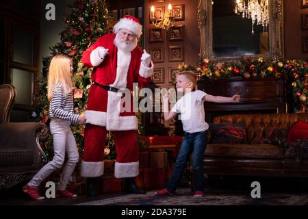 Les enfants et le Père Noël écoutent de la musique et dansent à la maison près de l'arbre de Noël. Fête familiale sœur et frère célébrant Noël Banque D'Images