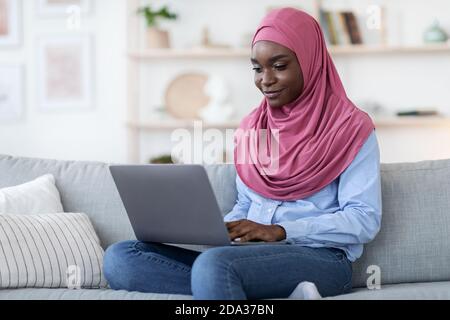 Communication en ligne. Femme musulmane noire souriante en foulard sur ordinateur portable à la maison Banque D'Images