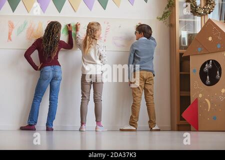 Vue arrière d'un groupe multiethnique d'enfants tirant sur les murs tout en appréciant la classe d'art à l'école, l'espace de copie Banque D'Images