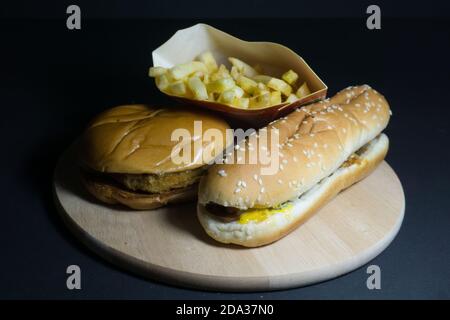 Frites avec hamburger et hot dog sur plateau en bois sur fond noir Banque D'Images