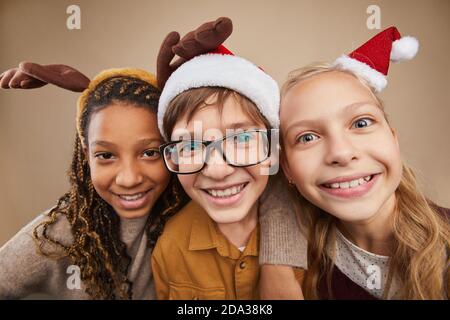 Gros plan portrait de trois enfants portant des costumes de Noël et souriant à l'appareil photo tout en se tenant contre l'arrière-plan en studio Banque D'Images