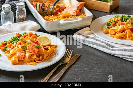 pâtes crémeuses avec filet de saumon servi avec des petits pois et des carottes sur une plaque Banque D'Images