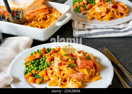 pâtes crémeuses avec filet de saumon servi avec des petits pois et des carottes sur une plaque Banque D'Images