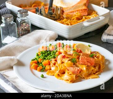 pâtes crémeuses avec filet de saumon servi avec des petits pois et des carottes sur une plaque Banque D'Images