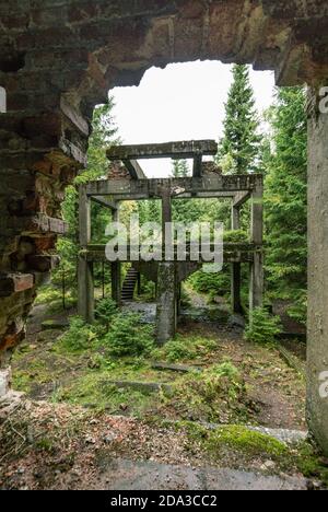 Tour minière et usine de traitement de l'étain Rolava-Sauersac vu à travers un trou dans un mur de briques Banque D'Images