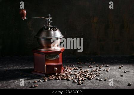 Moulin à café en bois nostalgique et grains de café torréfiés dans une lumière latérale sur fond rustique foncé avec espace de copie, mise au point sélectionnée Banque D'Images