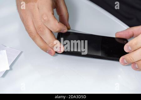 un homme enlève l'ancien verre protecteur du téléphone pour le remplacer par un nouveau. le processus de changer le verre protecteur d'un smartphone Banque D'Images
