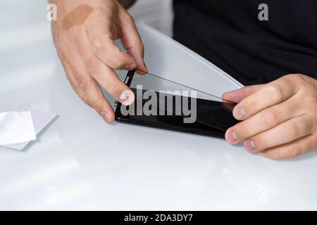 un homme retire l'ancien verre protecteur du téléphone pour le remplacer par un nouveau. Banque D'Images