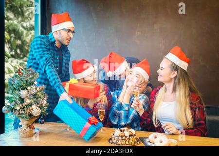 Groupe d'amis avec des chapeaux de père Noël célébrant Noël en partageant cadeaux et champagne à la maison Banque D'Images