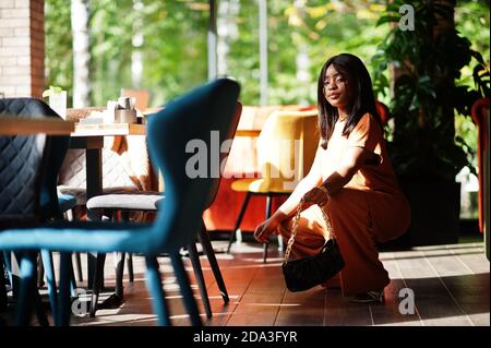 Portrait de la beauté jeune femme noire, porter une tenue orange, poser au restaurant. Banque D'Images