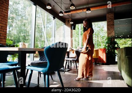 Portrait de la beauté jeune femme noire, porter une tenue orange, poser au restaurant. Banque D'Images