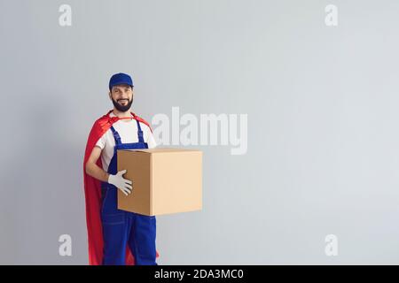 Un messager masculin souriant portant un uniforme de travail porte un manteau rouge de super-héros et livre les marchandises rapidement. Banque D'Images