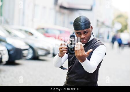 Jeune photographe afro-américain professionnel tenant un appareil photo professionnel avec un équipement professionnel. Afro cameraman portant le duraq noir faire des vidéos. Banque D'Images