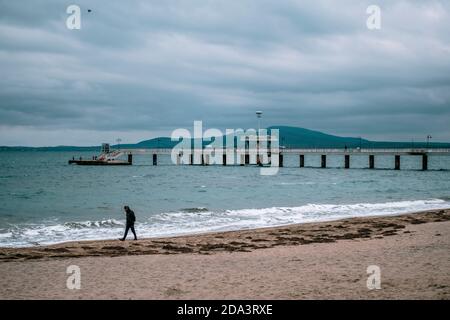 Une personne marchant seule sur une plage vide à Burgas, Bulgarie. Hiver automne saison, temps froid. Temps nuageux, pont de mer en arrière-plan. Haute q Banque D'Images