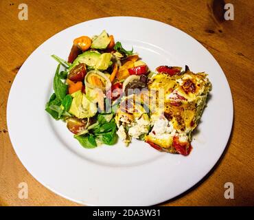 Fromage de chèvre Frittata fait avec des courgettes de poivre rouge et des œufs avec salade mélangée sur assiette blanche Banque D'Images
