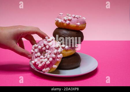 Gros plan d'une main ramassant un beignet d'une assiette blanche de beignets roses avec cumin et chocolat couvert. Photographie horizontale Banque D'Images