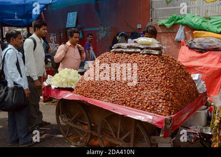 Delhi, Inde - avril, 2014: Grand tas de fruits secs sur une charrette en bois sur roues . Homme vendant des aliments sucrés sur le marché de rue Banque D'Images