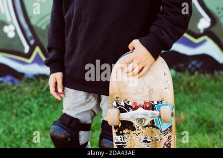 Gros plan d'un garçon patineur avec un vieux skateboard devant une fresque graffiti Banque D'Images