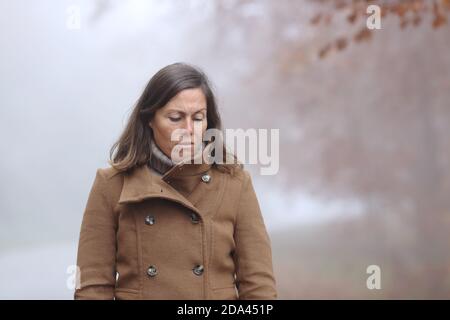 Triste femme d'âge moyen regardant en marchant dans une forêt en automne un jour brumeux Banque D'Images