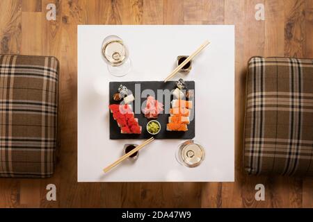 Un ensemble de sushis colorés sur une table blanche avec vin dans une chambre confortable. Banque D'Images