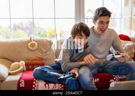 Deux jeunes frères assis sur le canapé à la maison, souriant tout en jouant à des jeux d'ordinateur ensemble Banque D'Images