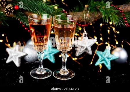 Décoration du nouvel an et de Noël. Des verres pour champagne, des jouets pour l'arbre de Noël se tiennent sur la table à l'avant dans le noir, magnifique bokeh sur le dos Banque D'Images