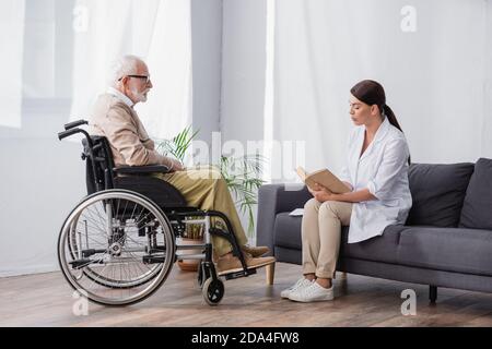 travailleur social lisant le livre à l'homme handicapé en fauteuil roulant à accueil Banque D'Images