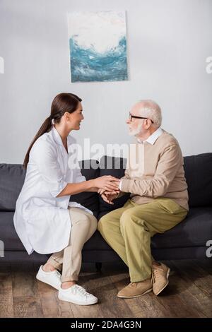 vue latérale de l'infirmière gériatrique et de l'homme âgé parlant pendant salon sur canapé Banque D'Images