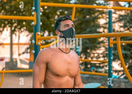 Jeune homme latino en pantalon noir et masque faisant des exercices dans un parc de calisthéniques sans t-shirt Banque D'Images