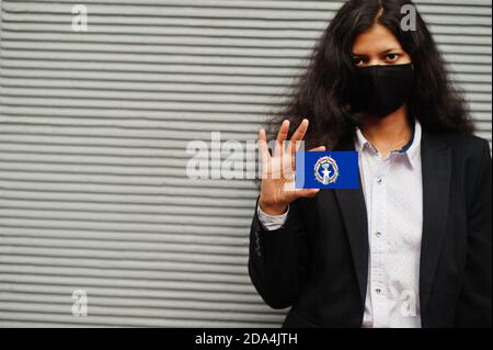 La femme asiatique en tenue officielle et masque noir protège le visage porte le drapeau des îles Mariannes du Nord à la main sur fond gris. Coronavirus au conc. Du pays Banque D'Images