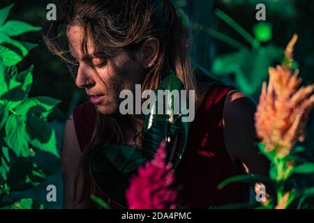 Portrait rapproché d'une femme caucasienne aux yeux bruns portant une robe rouge entourée par les plantes Banque D'Images