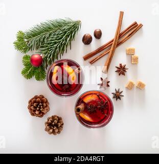 Vin chaud, boisson alcoolisée réchauffant l'hiver, deux tasses en verre, ingrédients orange et épices et décoration d'arbre de Noël sur fond blanc, vue du dessus. Banque D'Images