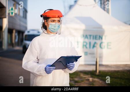 Ambulancier portant un équipement de protection individuelle, un PPE tenant une plieuse à l'intérieur Avant de l'USI isolement de l'hôpital rt-PCR drive site de test, COVID-19 Banque D'Images