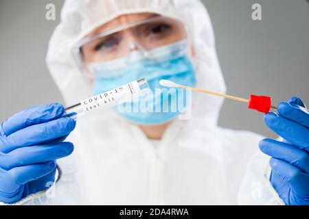 Technologue en soins médicaux tenant le kit de prélèvement d'écouvillons COVID-19, portant des gants de protection PPE blancs, tube à essai pour les tests PCR Banque D'Images