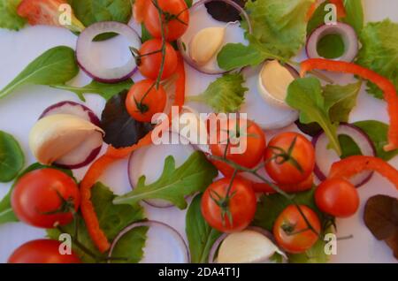 Ingrédients de salade colorés motif composé de tomates, de ruccola, de rondelles d'oignon violet, de poivron rouge, de piment, d'ail, de tranches de concombre et de basilic sur blanc Banque D'Images