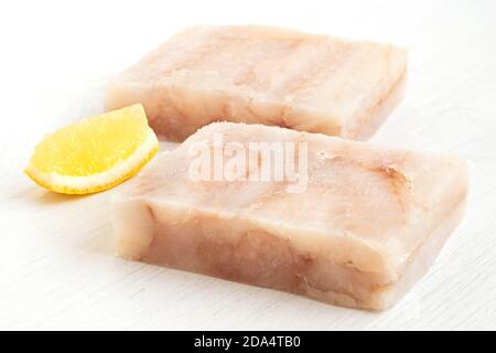 Deux blocs de filet de polock surgelé rapide avec un coin de citron isolé sur blanc. Banque D'Images