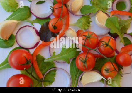 Ingrédients de salade colorés motif composé de tomates, de ruccola, de rondelles d'oignon violet, de poivron rouge, de piment, d'ail, de tranches de concombre et de basilic sur blanc Banque D'Images
