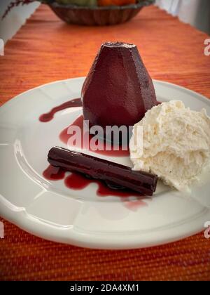 Poires composées dans du vin rouge, sauce au vin, bâton de cannelle et glace à la vanille sur une assiette blanche Banque D'Images