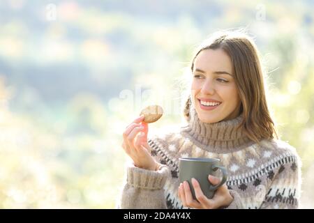 Bonne femme mangeant des biscuits et buvant du café dans la montagne en hiver Banque D'Images