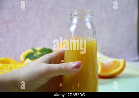 Femme à la main avec du jus d'orange fraîchement pressé dans une bouteille et orandes sur fond couleur Banque D'Images